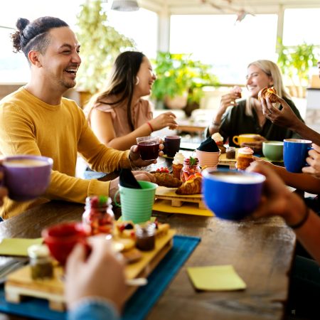 Group of diverse friends having breakfast and talking at coffee bar restaurant